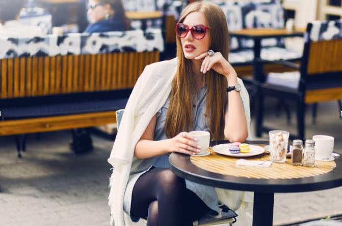 A blonde woman wearing one of the best bridal brunch outfits while having coffee and breakfast at a restaurant.