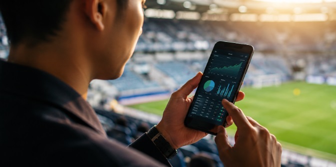 Man reviews financial charts on a smartphone at a stadium